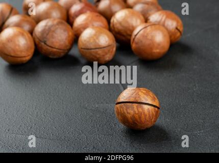 Scattered macadamia nuts in their shells on a dark background Stock Photo