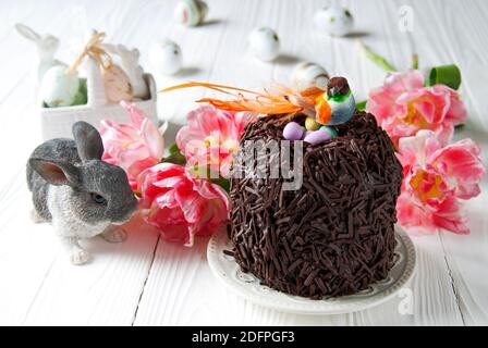 Easter chocolate cake and bird sitting in the nest. Little orange bird, colored eggs and grey rabbit on a background of Easter’s décor Stock Photo