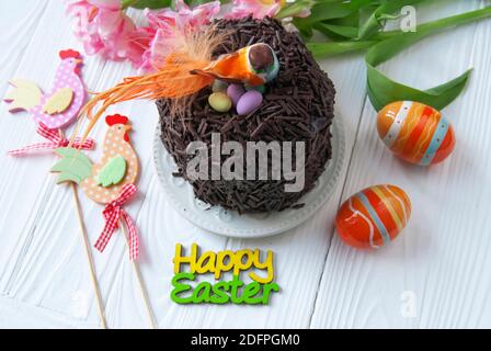 Easter chocolate cake and bird sitting in the nest. Little orange bird, colored eggs and text on a background of Easter’s décor Stock Photo