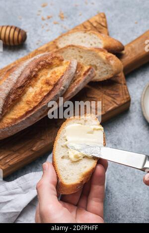 Spreading butter on slice of baguette bread. Bread and butter Stock Photo