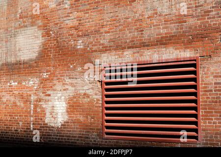 Angled view of weathered brick wall of an old industrial building with large HVAC exhaust vent painted red, horizontal aspect Stock Photo