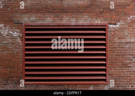 Exterior red brick wall with large painted industrial vent, weathered commercial building, horizontal aspect Stock Photo