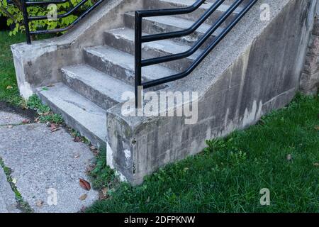 Weathered concrete stairs with heavy black pipe railing, grassy yard and concrete walkway, horizontal aspect Stock Photo