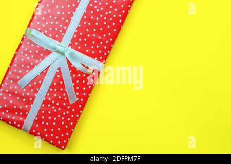 Gift box with copy space. Red rectangular box in a festive wrapping on a yellow background. Box with a white bow top view. Holiday surprise. Stock Photo
