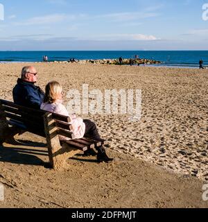 Poole Dorset UK, December 06 2020,  Senior Older Man and Woman Couple Sitting On A Wooden Bench Relaxing Looking Out To Sea Stock Photo