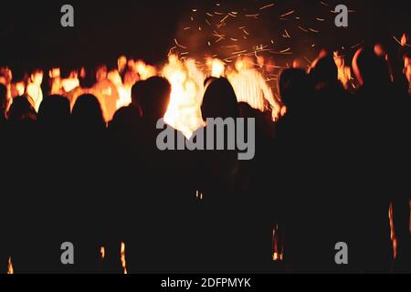 Moody and atmospheric image with people silhouetted against a fire on the beach during a cold summer night. Stock Photo