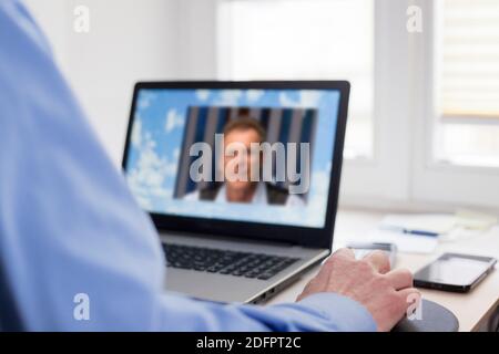 Two businessman talking online in a business meeting with laptop - selective focus on the hand in the foreground Stock Photo