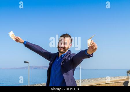 Cheerful attractive bearded young man holding 50 euro cash banknotes smiling happy isolated on blue sky background. Stock Photo