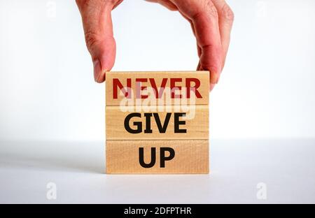 Never give up symbol. Male hand placing a block with word 'never' on top of a blocks tower with words 'never give up'. Beautiful white background. Cop Stock Photo