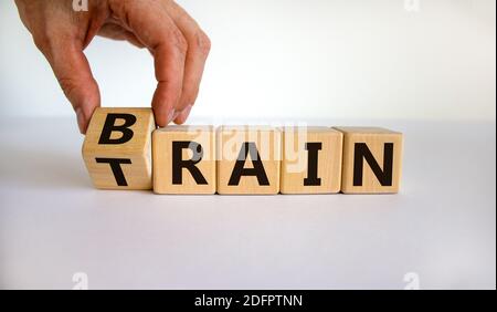 Train your brain. Hand turns a cube and changes the word 'train' to 'brain' on wooden cubes. Beautiful white background, copy space. Business and trai Stock Photo