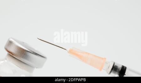 Vaccine vial with vaccination syringe, orange cannula and white background. Macro Stock Photo