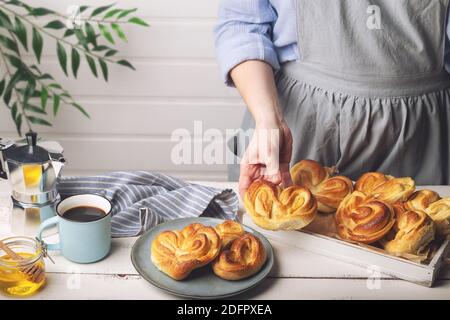 Homemade sweet buns in woman's hand. Serving breakfast at white rustic kitchen. Stock Photo