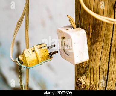 A yellow plug hangs half-inserted into a white ceramic socket on a wooden post in Hisor, Tajikistan – an improvised power connection. Stock Photo