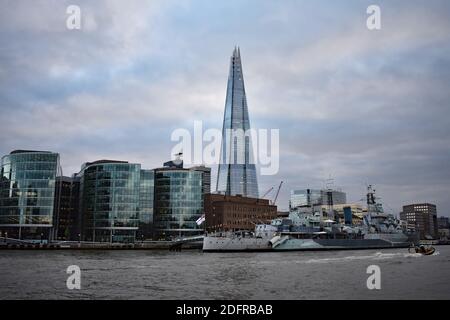 The Shard rises above buildings and the HMS Belfast warship museum from on the River Thames on an overcast day at dusk in London, UK Stock Photo