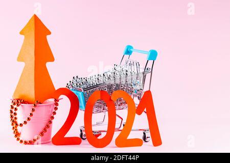 Red Christmas tree and the inscription 2021 in shopping cart. Christmas tree decorations in the shopping cart on a pink background. Holiday concept Stock Photo