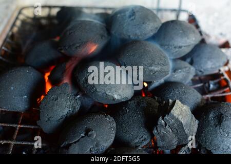 Pile of round briquettes of charcoal on grill, the fire just lit, preparation for  barbeque has just started, horizontal orientation, close up view Stock Photo