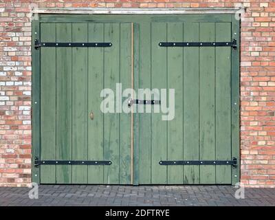 a green large door and a rectangular low window on a brick wall building Stock Photo