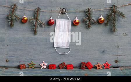 Corona and Christmas. A protective mask hangs next to Christmas tree balls, fir branches and gift packages Stock Photo