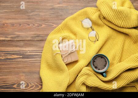 Stylish sweater with Christmas gift, cup of coffee and eyeglasses on wooden background Stock Photo