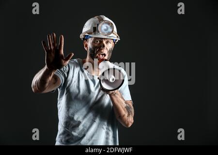 Protesting miner man with megaphone on dark background Stock Photo