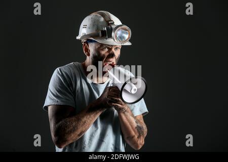Protesting miner man with megaphone on dark background Stock Photo