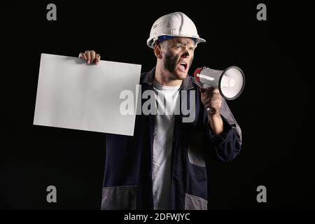Miner man with megaphone and placard on dark background Stock Photo