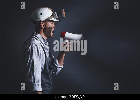 Protesting miner man with megaphone on dark background Stock Photo
