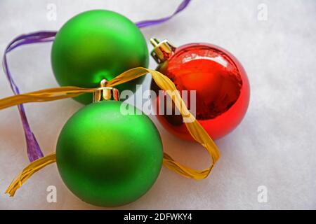 Two large green and one red Christmas ball ornament with gold and purple ribbon on grey background. Stock Photo