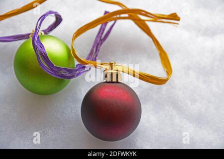 One red and one green large festive Christmas ball ornaments with gold and purple ribbon on grey background. Stock Photo