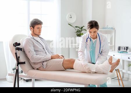 Doctor putting broken leg of young man in plaster Stock Photo