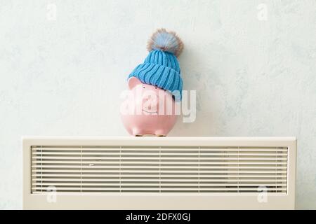 Piggy bank and hat on radiator. Concept of heating season Stock Photo