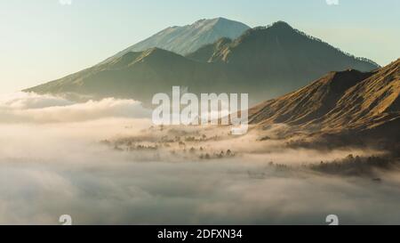 Sunrise view of mount Batur, Abang and Agung volcano in Bali from Pinggan village. Beautiful sunrise and low clouds. Layered minimalist landscape. Stock Photo