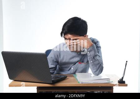 portrait of an Asian man with tired eyes working on computer reports and books. the concept of eye health looking at the monitor screen. office employ Stock Photo