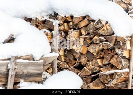 close-up of chopped wooden firewood, powdered with snow, stand in even rows on the street, prepared for heating the stove in the winter Stock Photo