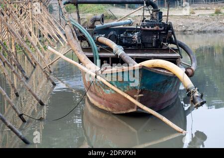 Old dredger bounded beside the bamboo bridge on a small river in Bangladesh Stock Photo