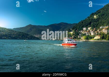 Como Lake in city Como, Lombardy, Italy. Picturesque landscape with mountains and red vessel boat sailing on water Stock Photo