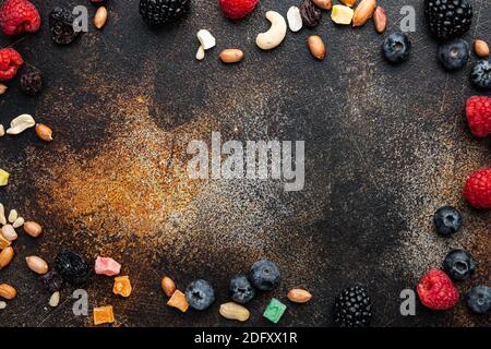 Frame made of mixed dried and raw ripe berry and fruit with nuts, flat lay with space for text, on old dark table Stock Photo