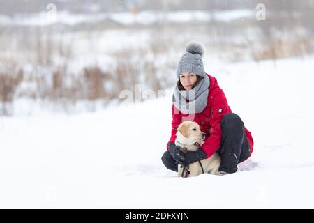 Young woman hugging Labrador puppy dog outdoor on snow in winter Stock Photo