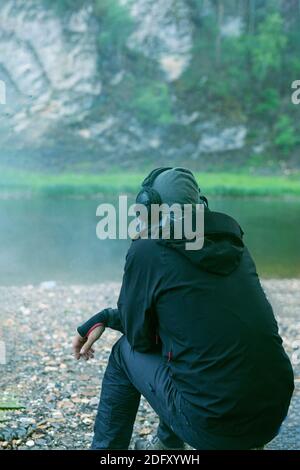 a lone man with headphones and cigarette is sitting on beach, view from back Stock Photo