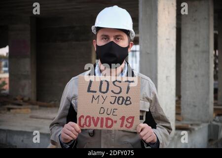 Engineer in mask and hardhat stands with placard Lost my job due covid-19 Stock Photo