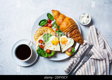Valentine's day breakfast concept. Sandwich with croissant, bagel, cream cheese and fried eggs hearts on a white plate. Stock Photo