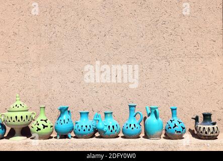 Traditional iranian souvenirs - colorful clay pot and jug, Yazd, Iran. Clay jugs of various shapes of green and blue colors on a shelf near the adobe Stock Photo