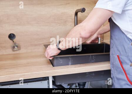 Male plumber installs a sink in the kitchen Stock Photo