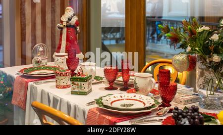 Festive Christmas decoration of the dinner table. Beautiful green red service, plate glass cup cutlery. Santa Claus in a red coat and a box with a gif Stock Photo