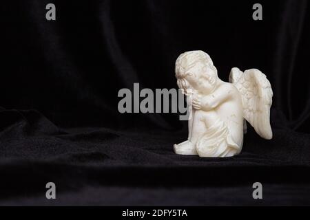 Small angel with wings on a black background, free space for text. Concept of memory of a person, funeral. Stock Photo