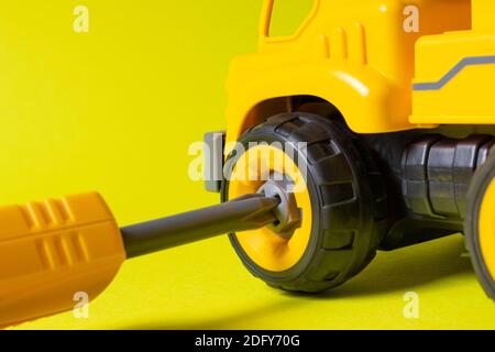 The screwdriver unscrews the wheel of the toy car on a yellow background. Toy machine, disassembled toy for children's development. Stock Photo