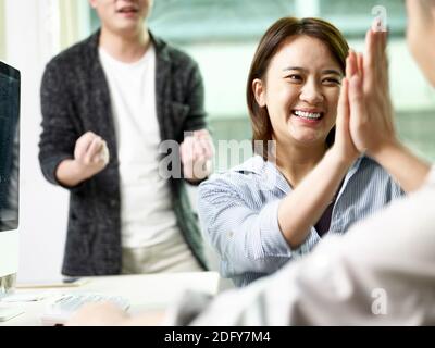 team of three asian business people giving hi-five celebrating achievement and success in office Stock Photo