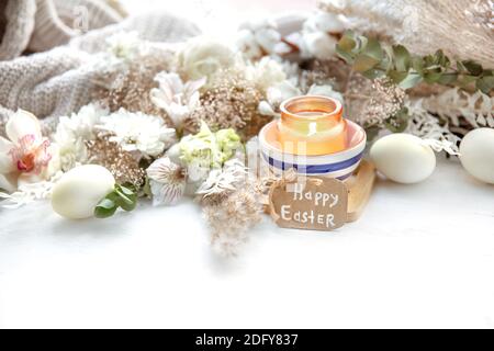 Spring still life with Easter eggs, burning candles in a pendant and flowers against the background of decor details. Easter holiday concept. Stock Photo