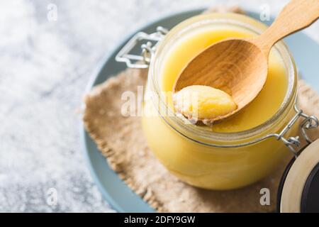 Ghee or clarified butter in jar and wooden spoon on gray table. Top view. Copyspace. Ghee butter have healthy fat and is a common cooking ingredient i Stock Photo