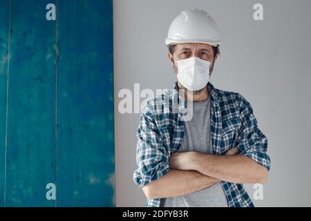Portrait of pensive construction engineer with protective face mask and white hard hat, copy space included Stock Photo